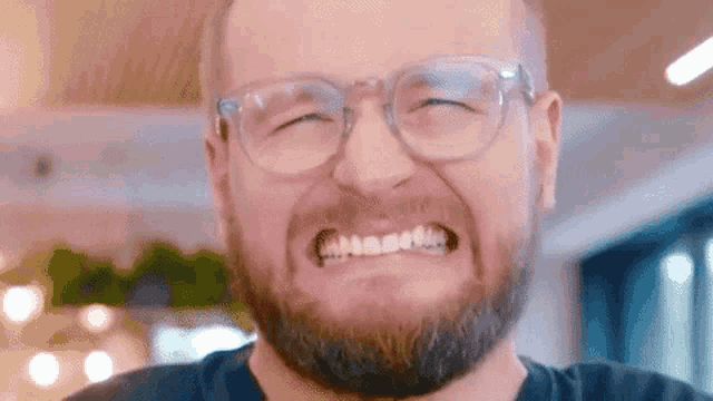 a man with a beard and glasses is making a funny face and smiling .