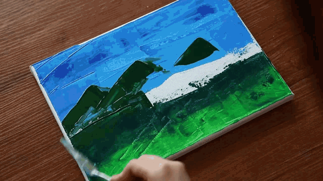 a person is painting a picture of mountains on a table