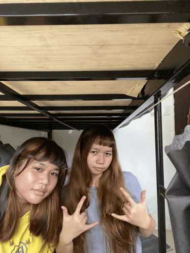 two girls standing under a bunk bed with one wearing a yellow shirt that says ' a ' on it