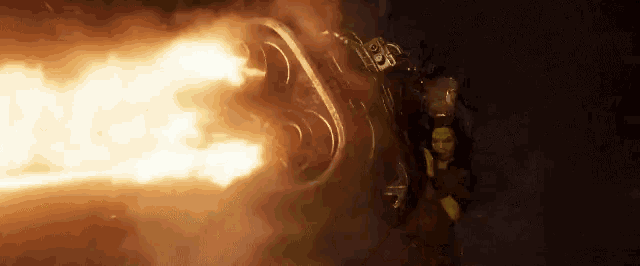 a woman in a yellow costume is holding a gun with flames coming out of it .