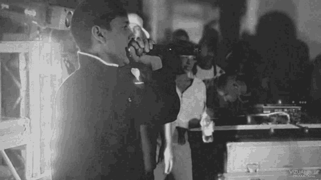 a black and white photo of a man singing in front of a crowd with the word visual on the bottom right corner