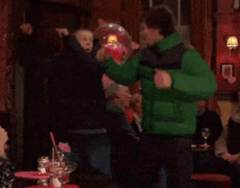 a man in a green jacket is dancing in a room with balloons and hearts