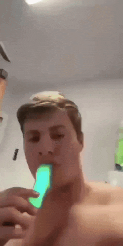 a man without a shirt is eating a green popsicle