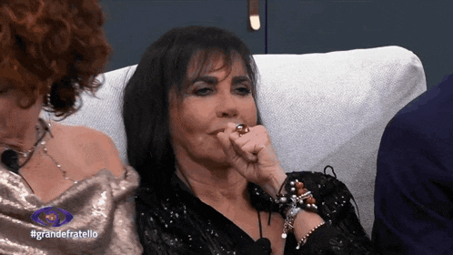 a woman with a ring on her finger is sitting on a couch in front of a sign that says grande fratello