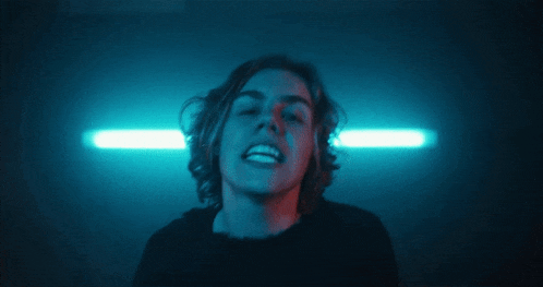 a young man with long hair is giving the middle finger in a dark room
