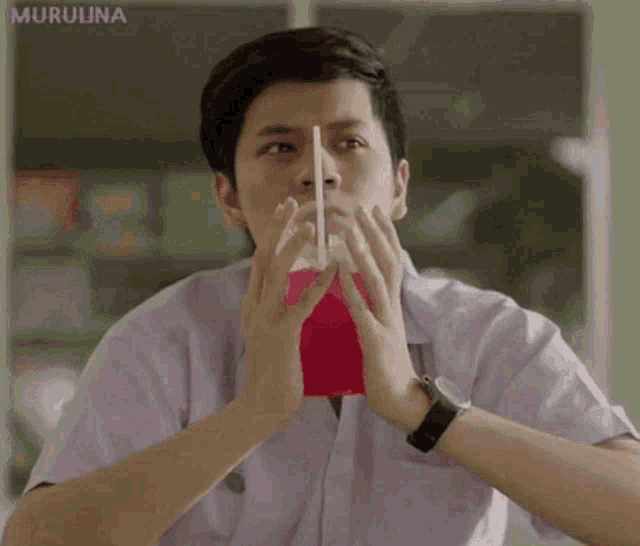 a man in a white shirt drinks from a red cup with a straw