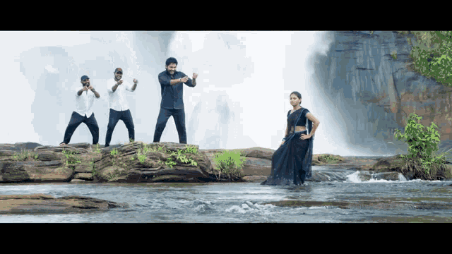 a woman in a black saree is standing in front of a waterfall with three men