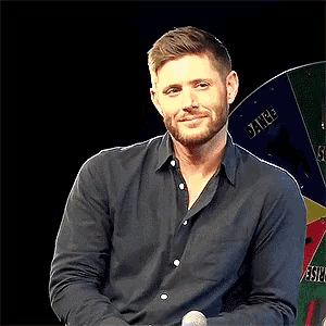 a man in a black shirt is smiling in front of a spinning wheel that says ' sauce ' on it