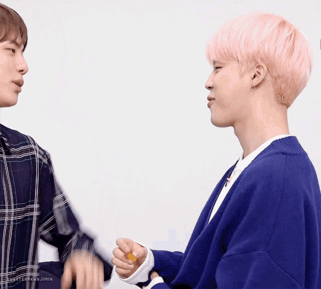 a man with pink hair holds another man 's hand while wearing a blue sweater