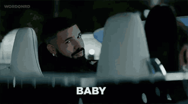 a man with a beard is sitting in the back seat of a car and talking to another man .