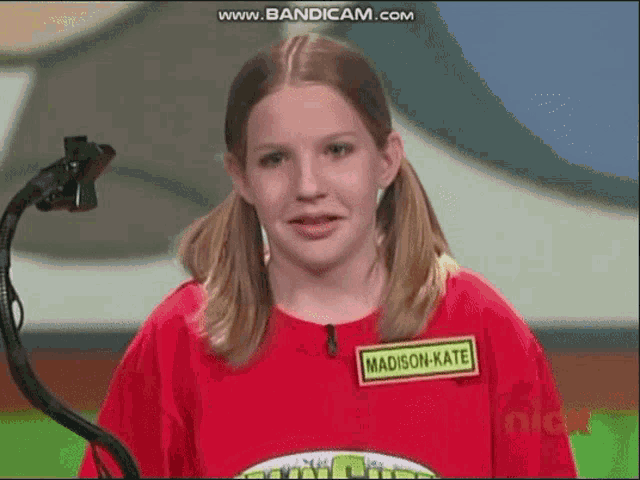 a young girl wearing a red shirt with a name tag that says madison kate is standing in front of a microphone .