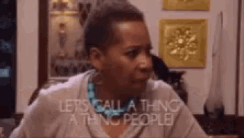 a woman is sitting at a table in a living room and talking to a cat .