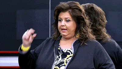 a woman in a black jacket is standing in front of a mirror and making a funny face