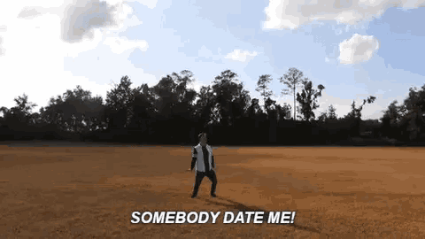 a man is standing in a field with the words `` somebody date me '' written on it .