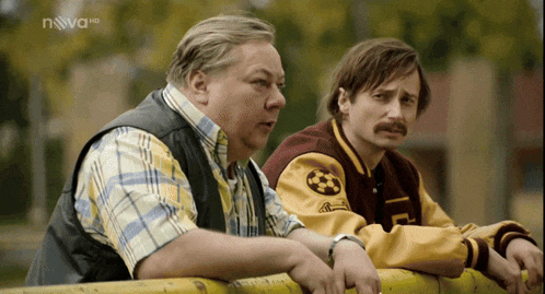 two men leaning over a yellow fence with nova hd written on the bottom right