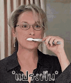 a woman wearing glasses is brushing her teeth with a toothbrush in front of a mirror .