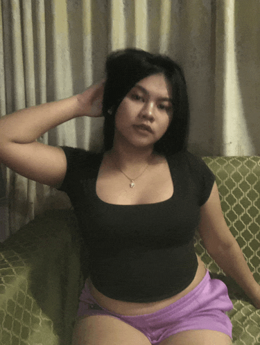 a woman in a black shirt and purple shorts is sitting on a couch