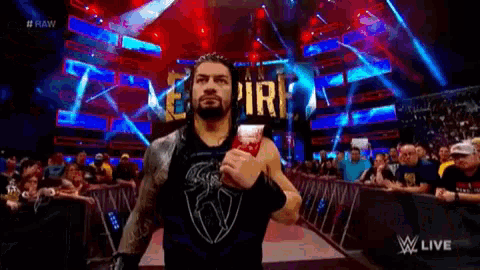 roman reigns is walking down the aisle of a wrestling ring holding a bottle of ice cream .