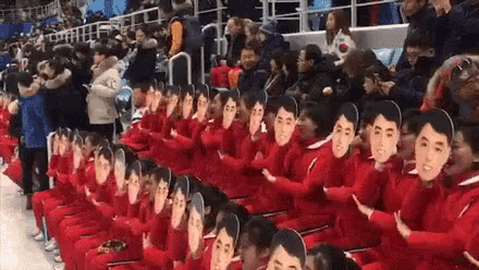 a group of people wearing red jackets and masks are sitting in a row in a stadium .