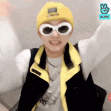 a young man wearing a yellow hat and sunglasses is standing with his arms outstretched .