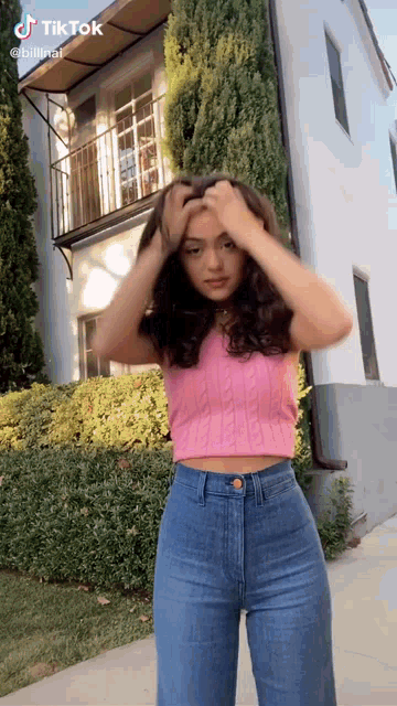 a woman wearing a pink crop top and blue jeans is standing in front of a white building .