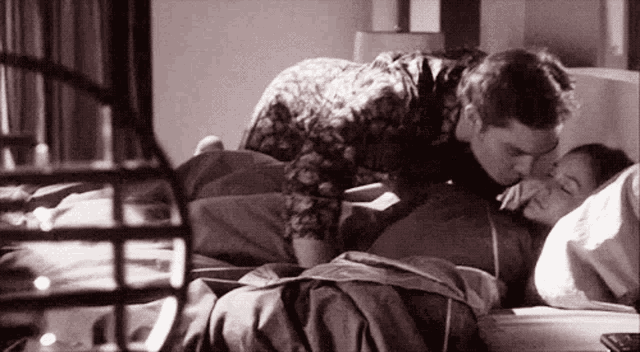 a man kisses a woman on the forehead while she sleeps