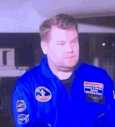 a man in a blue space suit with nasa patches on the sleeves