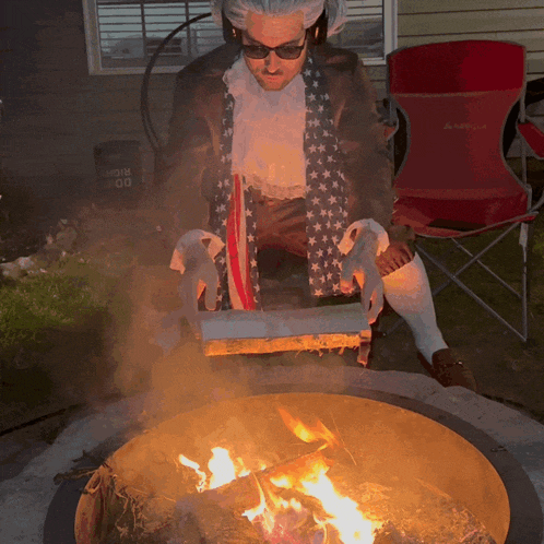 a man sitting in front of a fire pit with a red chair in the background that says arnold