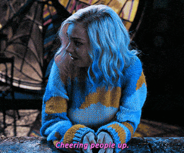a woman with blue hair is wearing a blue and yellow sweater that says cheering people up