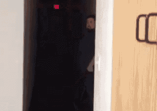 a man is standing in a dark room with a red exit sign on the wall
