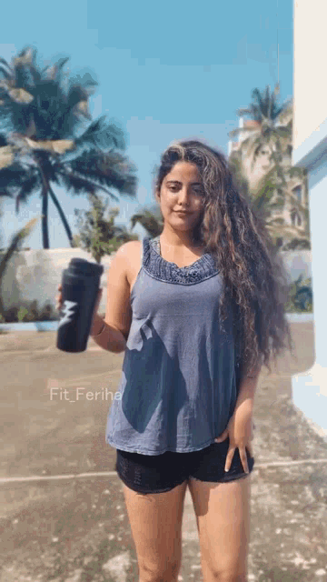 a woman in a blue tank top and black shorts is holding a black bottle that says fit ferihe