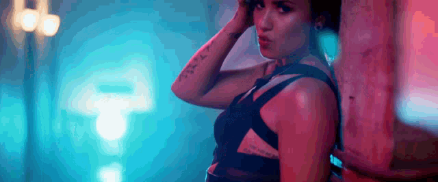 a woman with a tattoo on her arm is leaning against a wall .