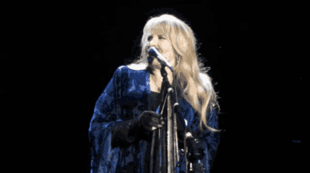 a woman singing into a microphone on a stage in a dark room