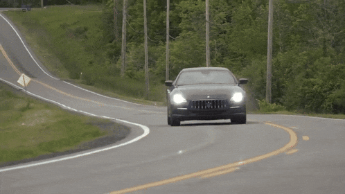 a black maserati is driving down a curvy country road