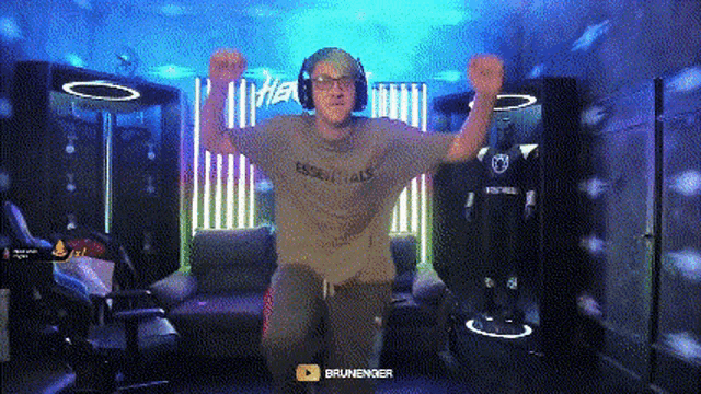 a man wearing headphones and a shirt that says essentials is dancing in a room with blue lights .