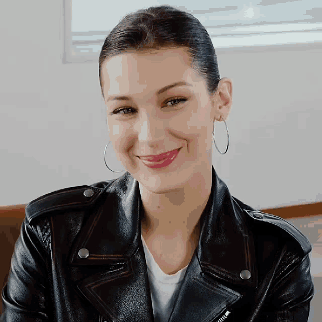a woman wearing hoop earrings and a leather jacket smiles
