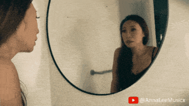 a woman looking at her reflection in a round mirror with a youtube play button
