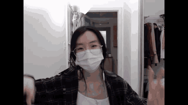 a woman wearing a mask and glasses stands in front of a closet