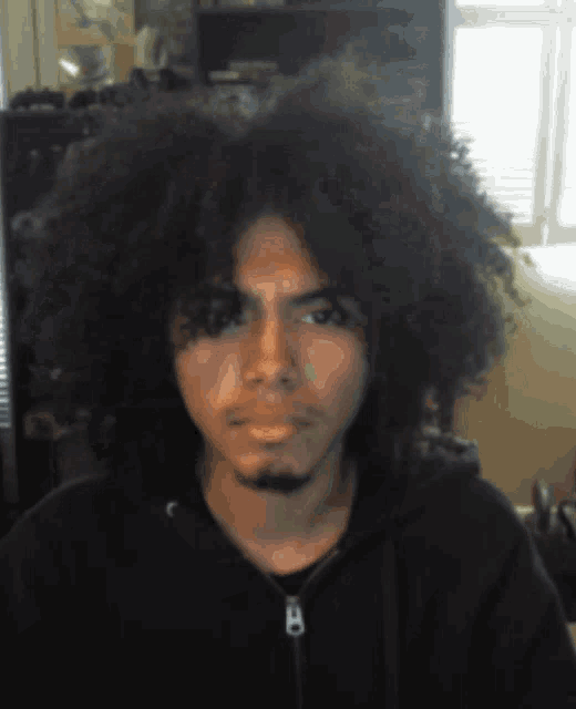 a man with a beard and a large afro is wearing a black hoodie with the letter b on it