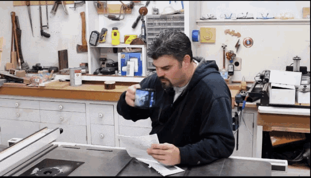 a man in a black hoodie is drinking from a cup