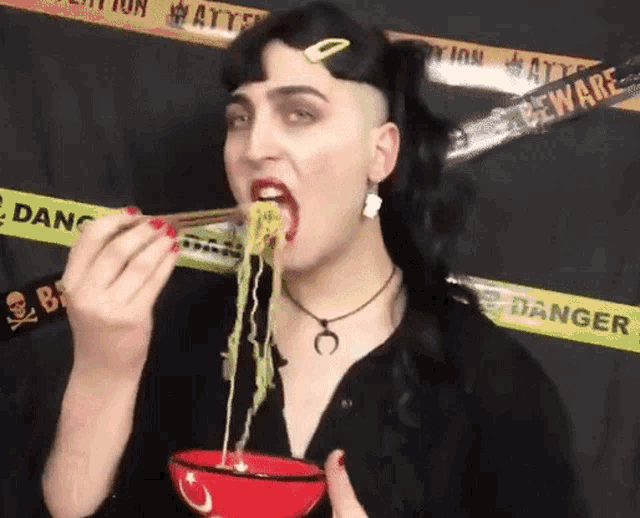 a woman eating noodles with chopsticks in front of a caution tape that says danger