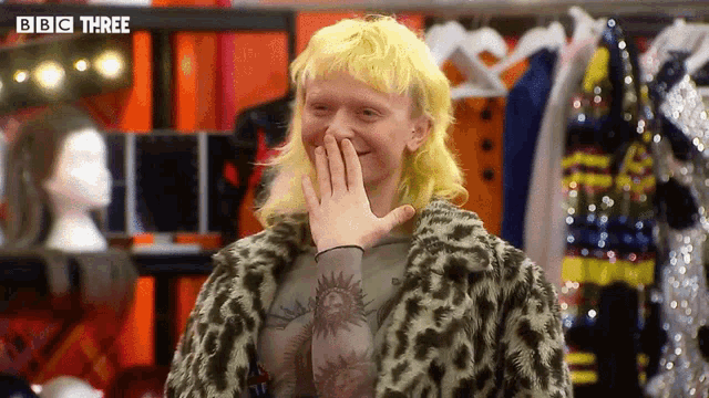 a man with yellow hair is covering his mouth with his hand .