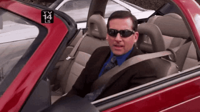 a man in a suit and tie is sitting in a red car with a tv 14 ls logo behind him .