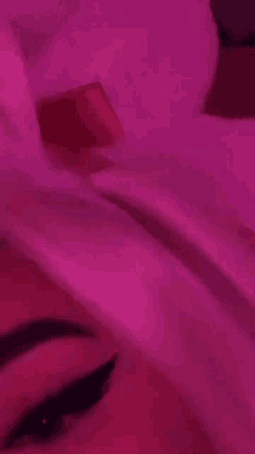 a woman is laying on a bed with a pink light on her face .