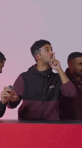 a man in a black and maroon jacket holds his finger to his nose