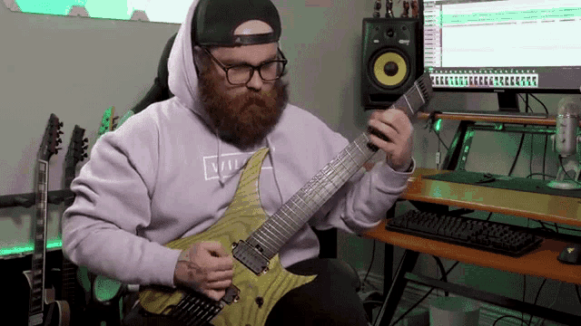 a man with a beard is playing a guitar in front of a computer