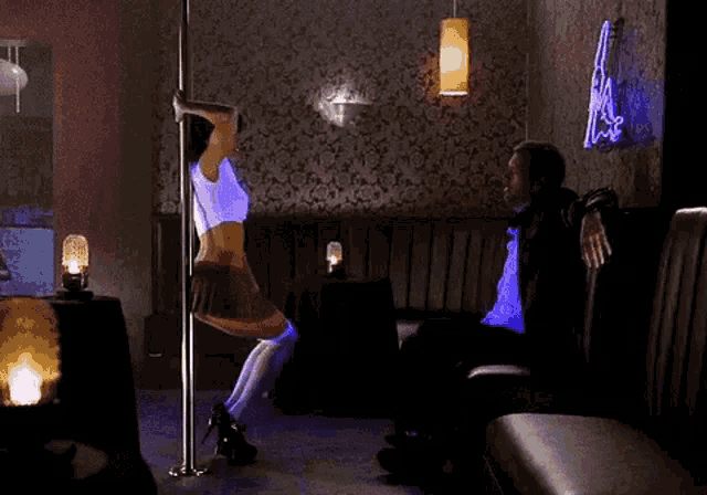 a woman is dancing on a pole while a man looks on .