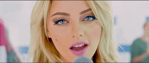 a blonde woman singing into a microphone with purple lipstick