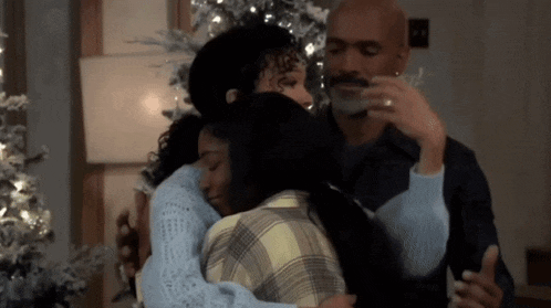 a group of people hugging each other in front of a christmas tree .