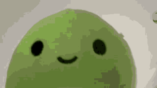 a green stuffed animal with a smile on its face is sitting on a table .
